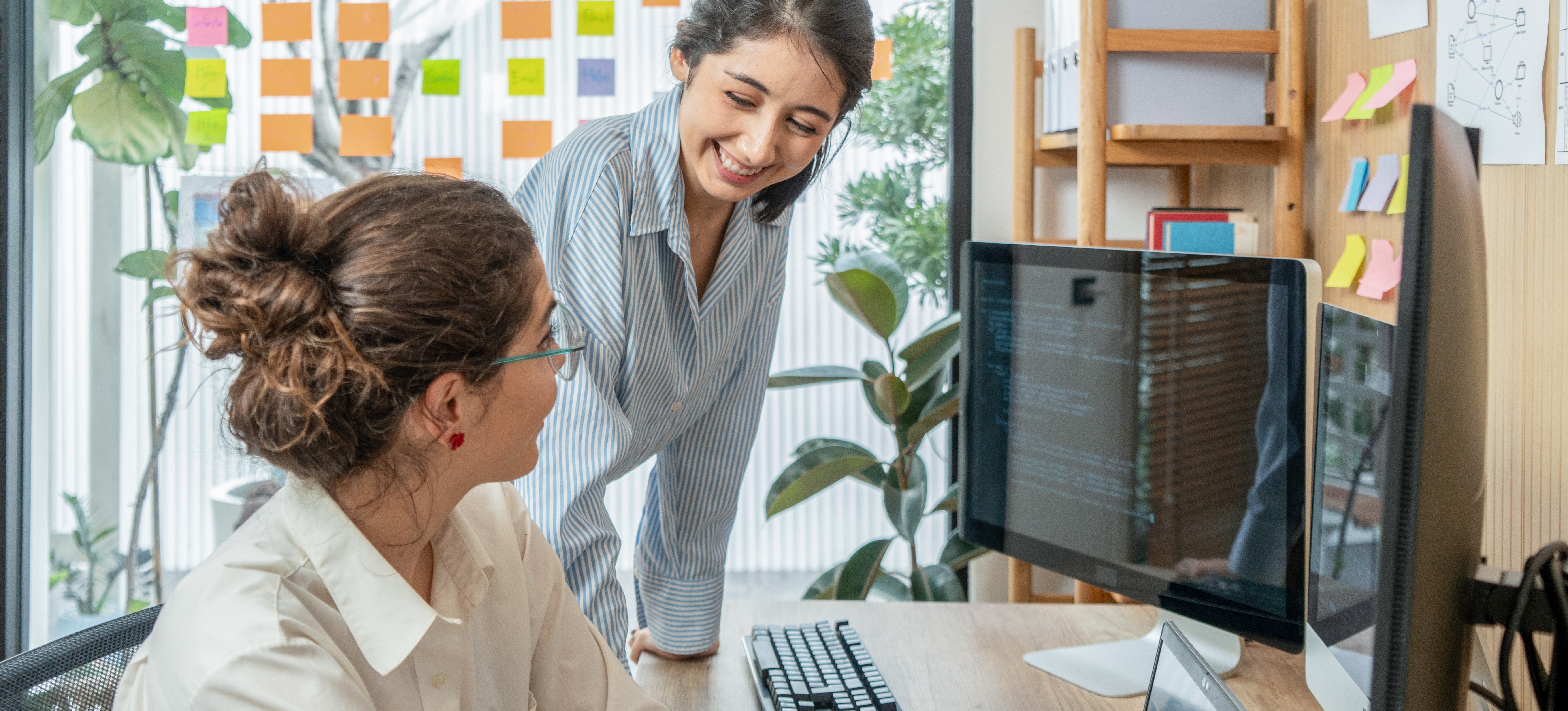 [Featured Image] DataOps and MLOps specialists in a workspace, interacting while reviewing code on their computer screens.
