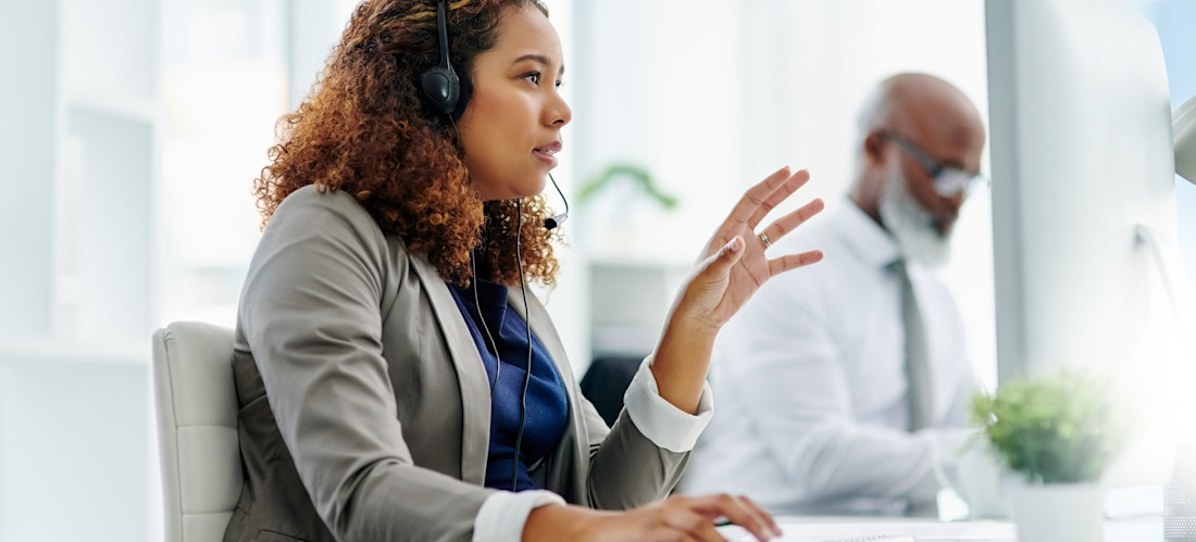 [Featured Image] An IT support specialist talking into a headset while sitting at a computer explaining troubleshooting options to a caller.
