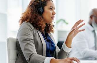 [Featured Image] A female IT support specialist talking into a headset while sitting at a computer explaining troubleshooting options to a caller.
