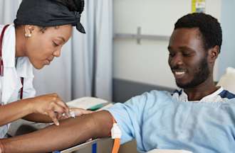 [Featured Image] A phlebotomist cares for a patient in a hospital.