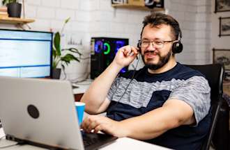 [Featured image] A front-end web developer sits at a computer wearing a headset and chats with a client about creating a new website.