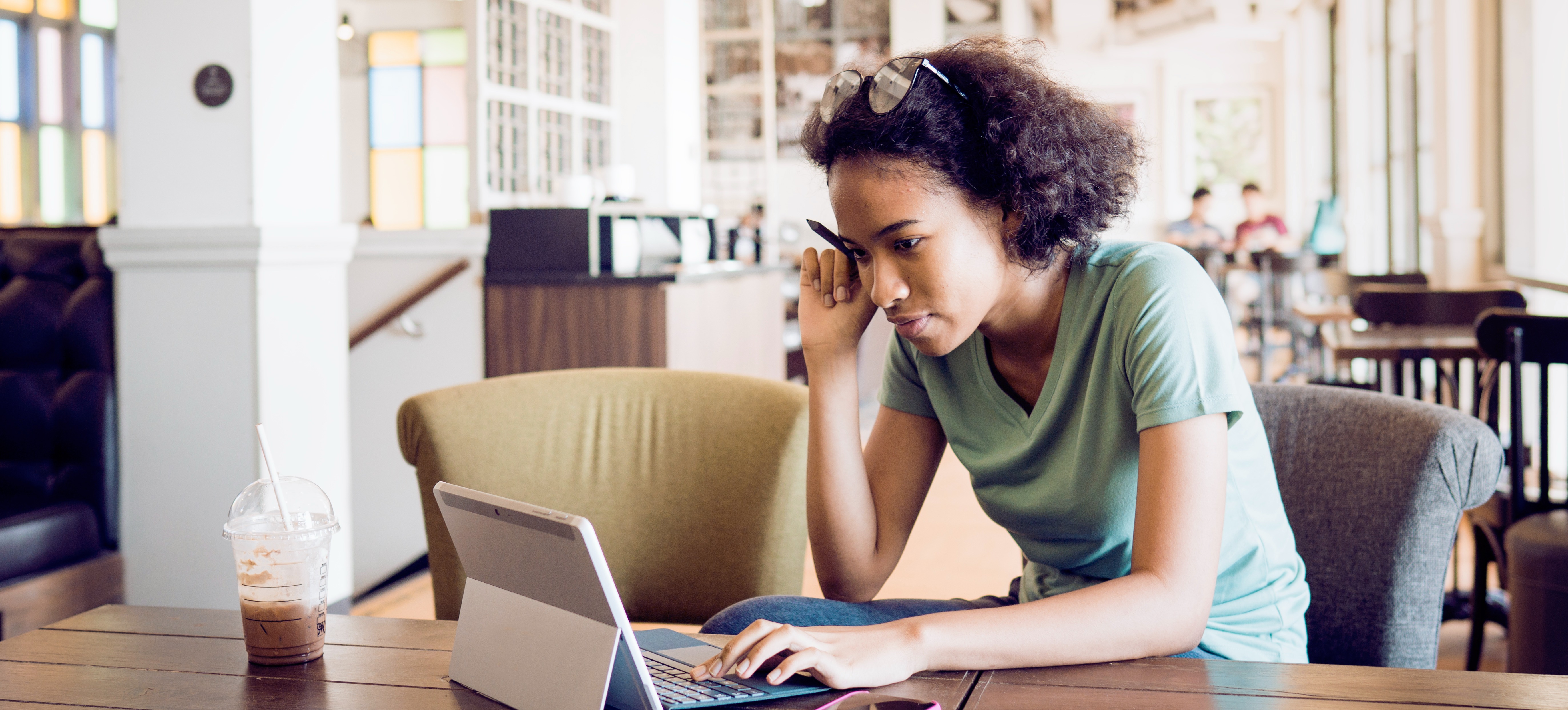 [Featured Image] A learner researches public health internships on their laptop while working at a wooden table in a sunny coffee shop