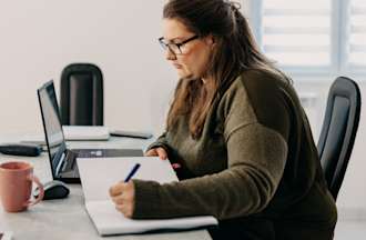 [Featured Image] A sustainability manager sits at her desk and conducts research on her company's environmental goals.  