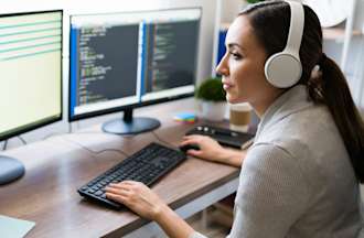 [Featured image] A person in headphones studies code on their home monitor. 