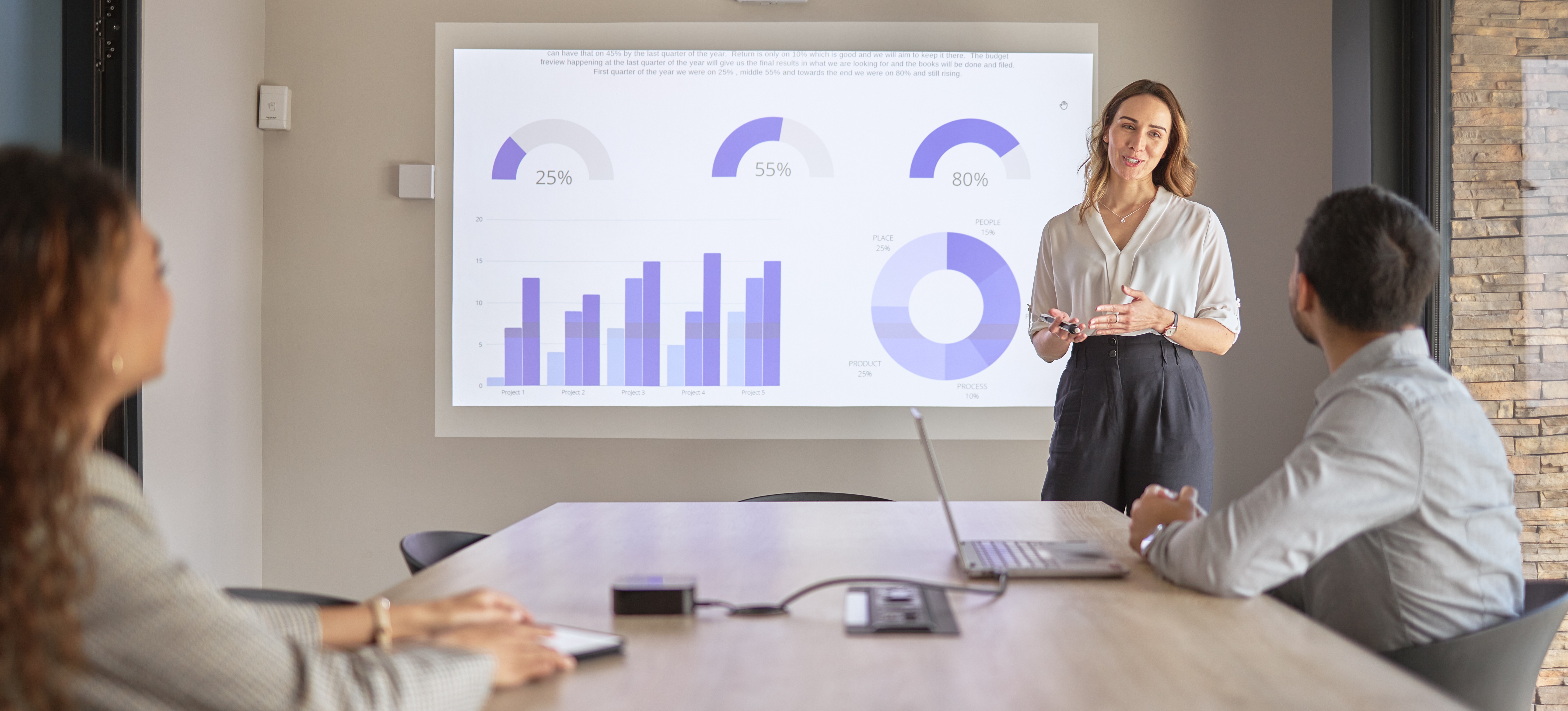 [Featured Image] A data visualization specialist presents visuals to two team leaders in a conference room, using the graphics to bring data analysis to life.  
