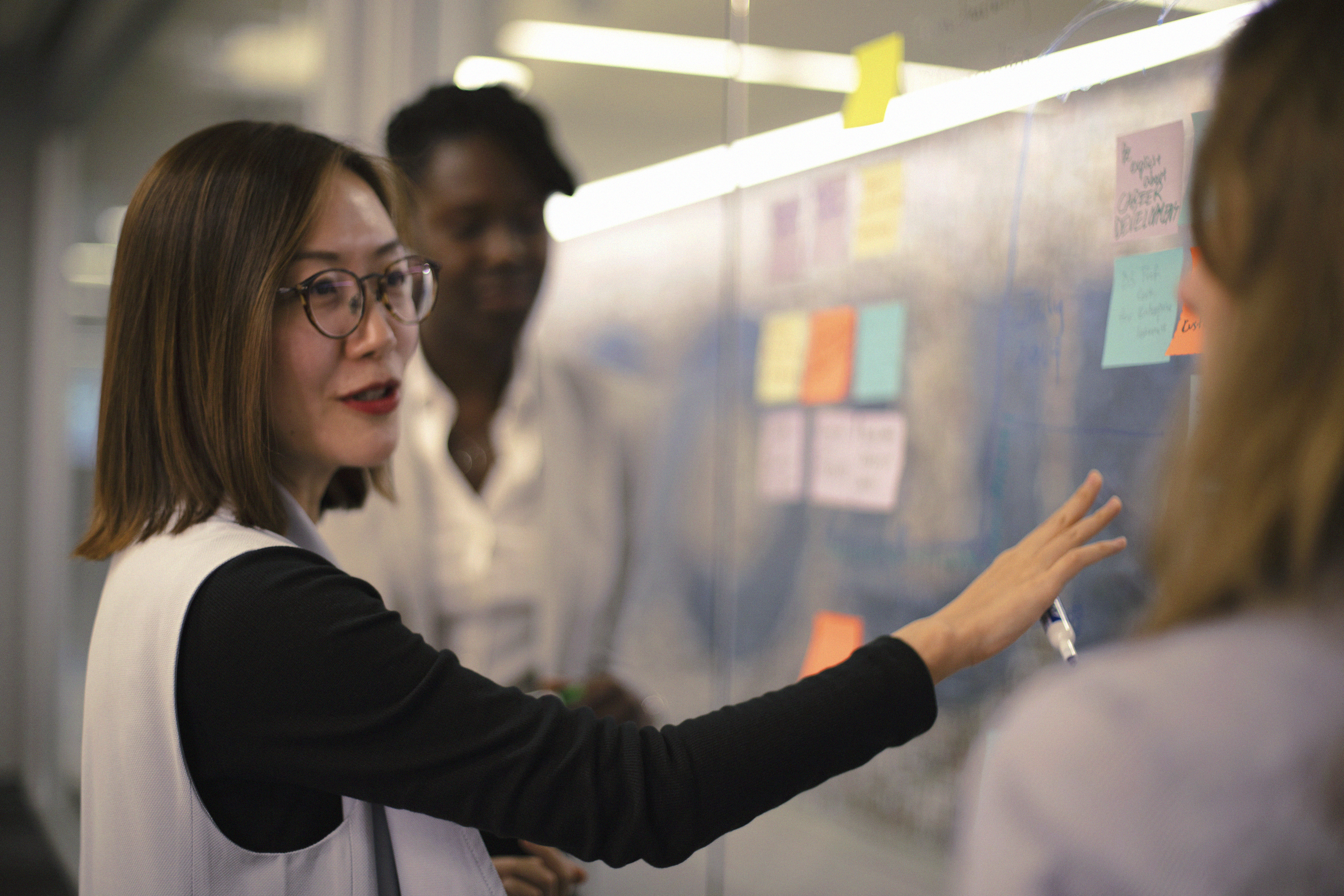 [Featured image] Three colleagues stand in front of a clear board with sticky notes on it discussing how to upload an email list to MailChimp.