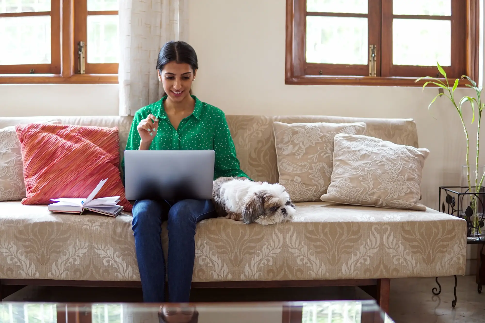 [Featured Image]: A person sits on a sofa next to a dog as they work one of their side hustles from home to earn extra money.
