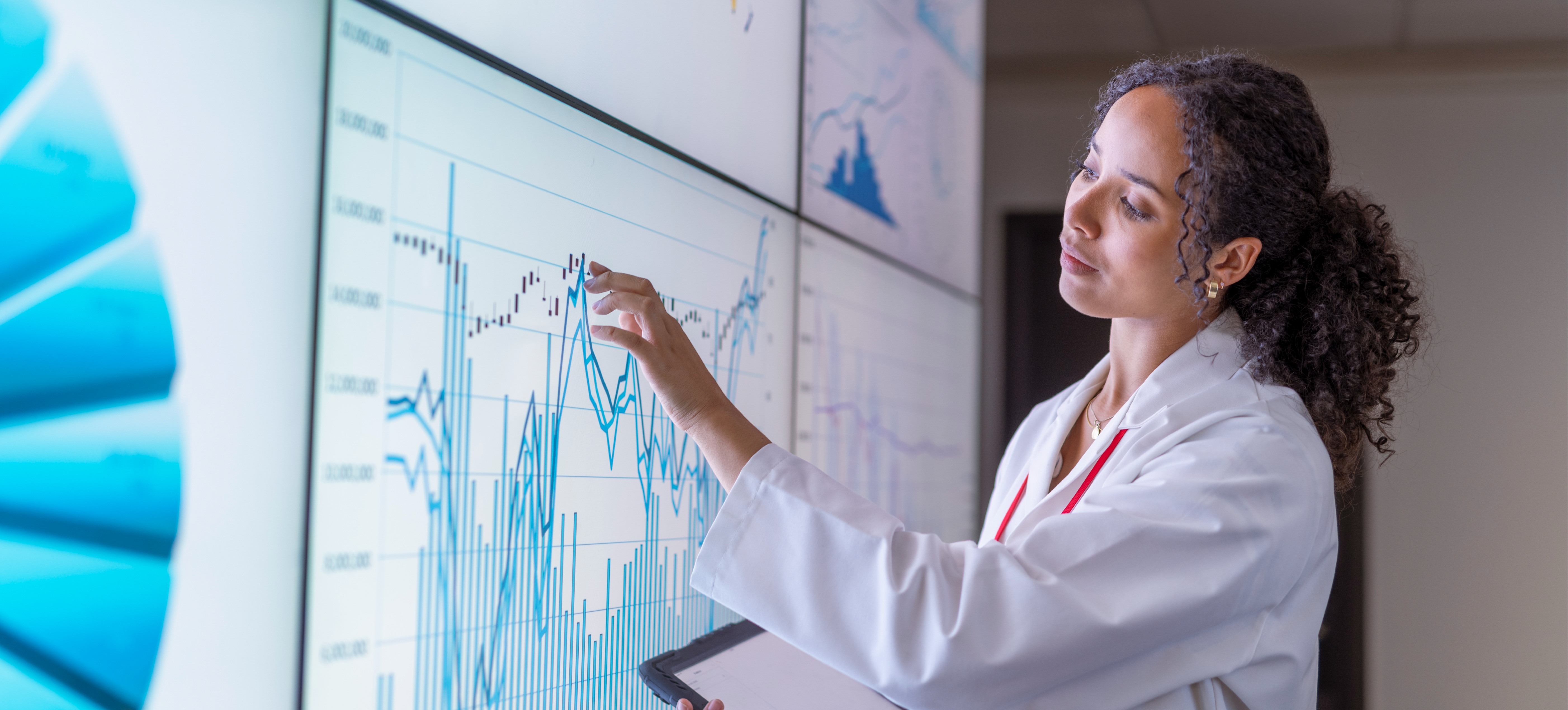 [Featured Image] A health informatics worker in a lab coat analyzes a chart with data.
