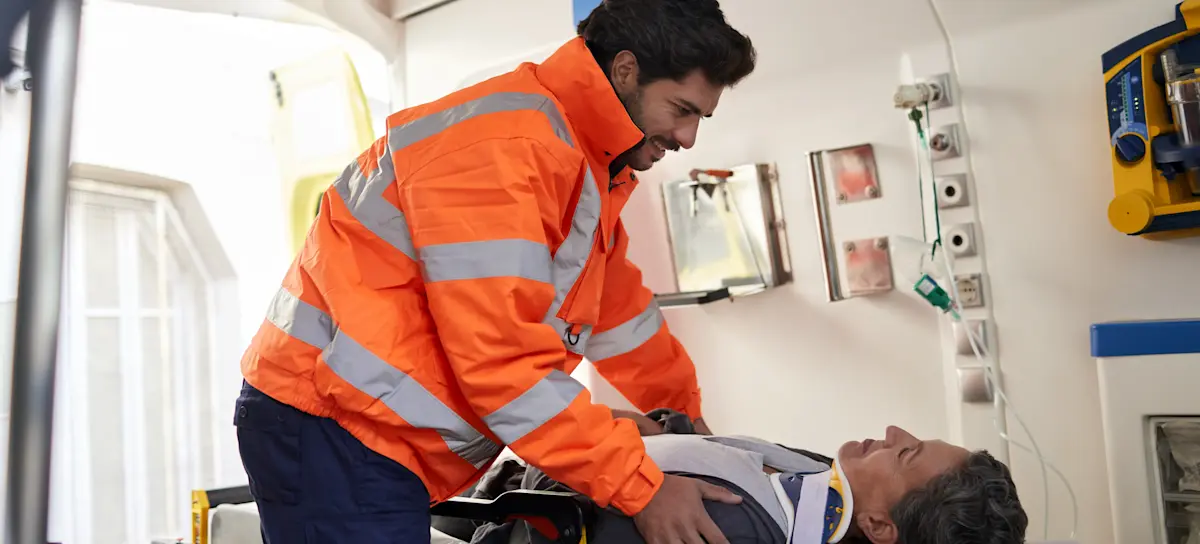 [Featured Image] A paramedic helps a patient on a stretcher in the back of an ambulance. 