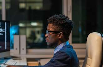 [Featured Image] A man wearing a blue sweater, and glasses collecting and analyzing data sitting in front of his computer. 