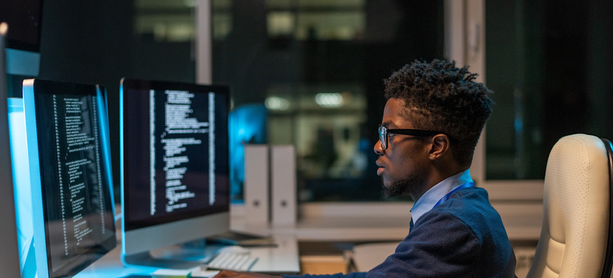 [Featured Image] A man wearing a blue sweater, and glasses collecting and analyzing data sitting in front of his computer. 
