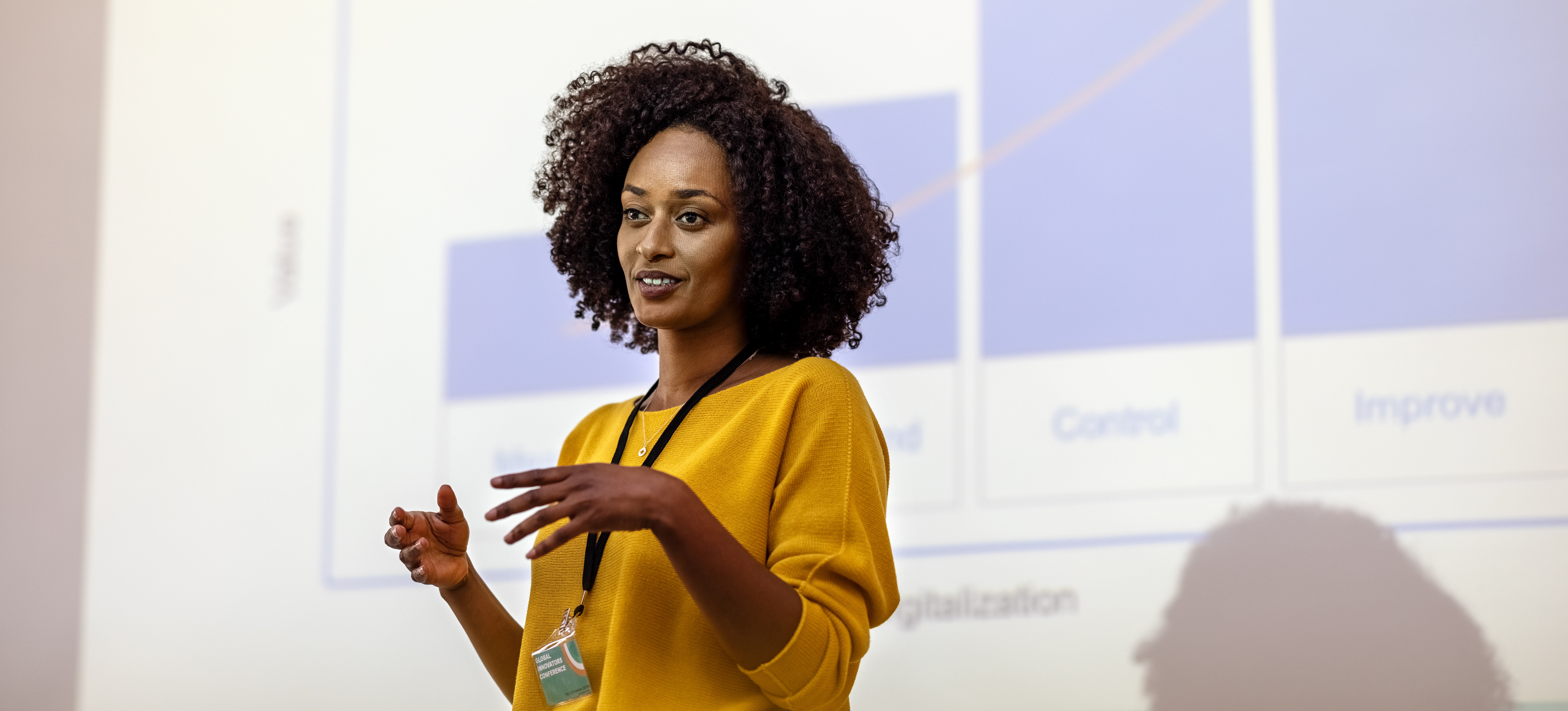[Featured Image] A data project manager stands before a screen and provides information to her team. 
