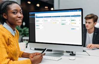 [Featured Image] A woman in a yellow sweater working as an IT project manager sits at her desk and uses her computer at work.