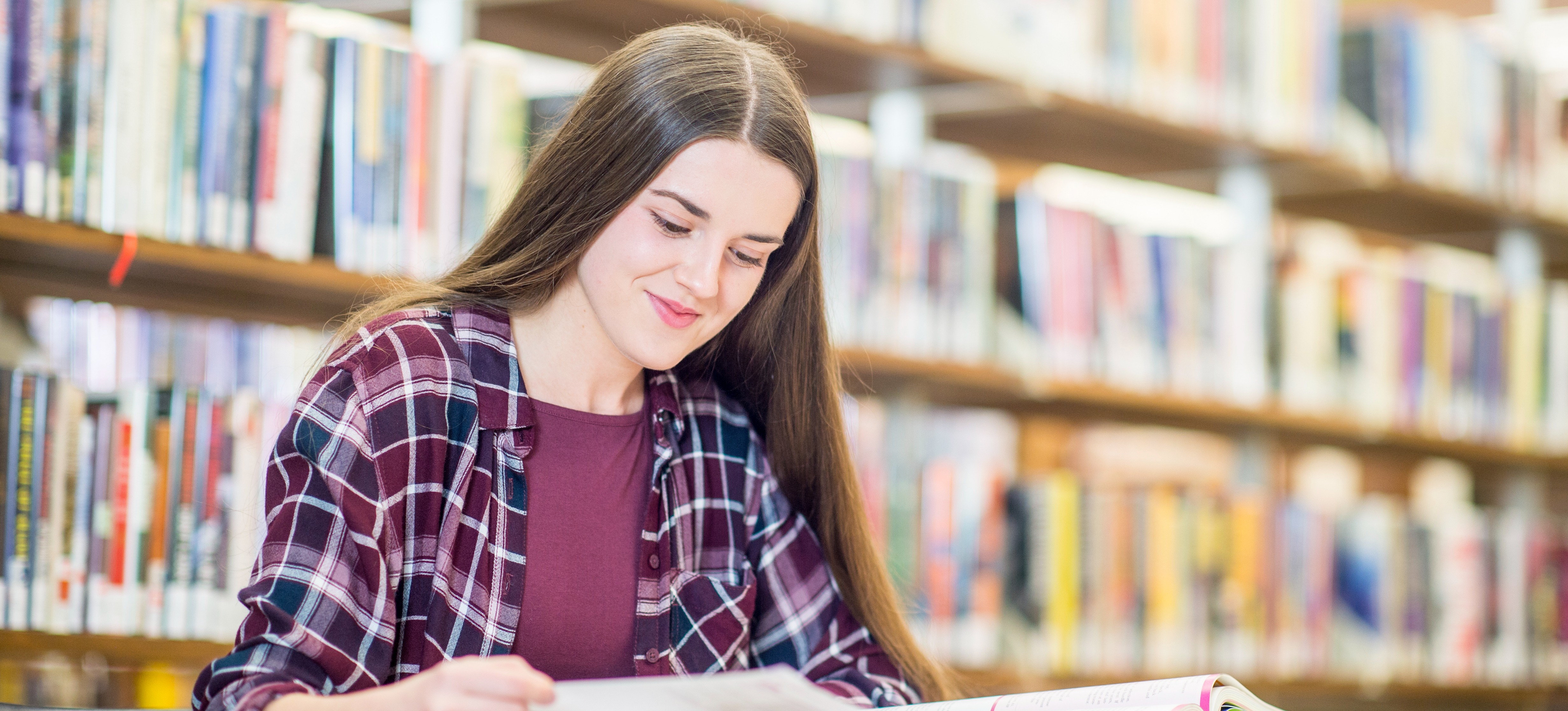 [Featured Image] A person in the library is smiling while studying in pursuit of their liberal arts degree.
