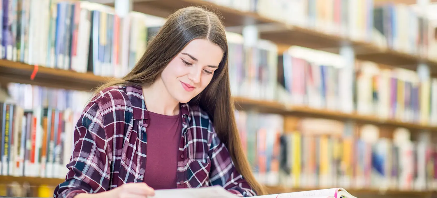 [Featured Image] A person in the library is smiling while studying in pursuit of their liberal arts degree.
