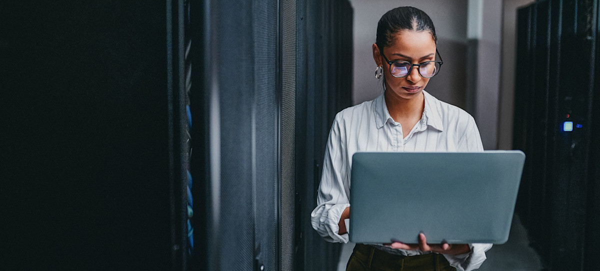 [Featured Image] A person works on a laptop computer in a server room.