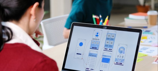 [Featured image] A graphic artist wearing a red sweater works on graphic designs on her laptop.
