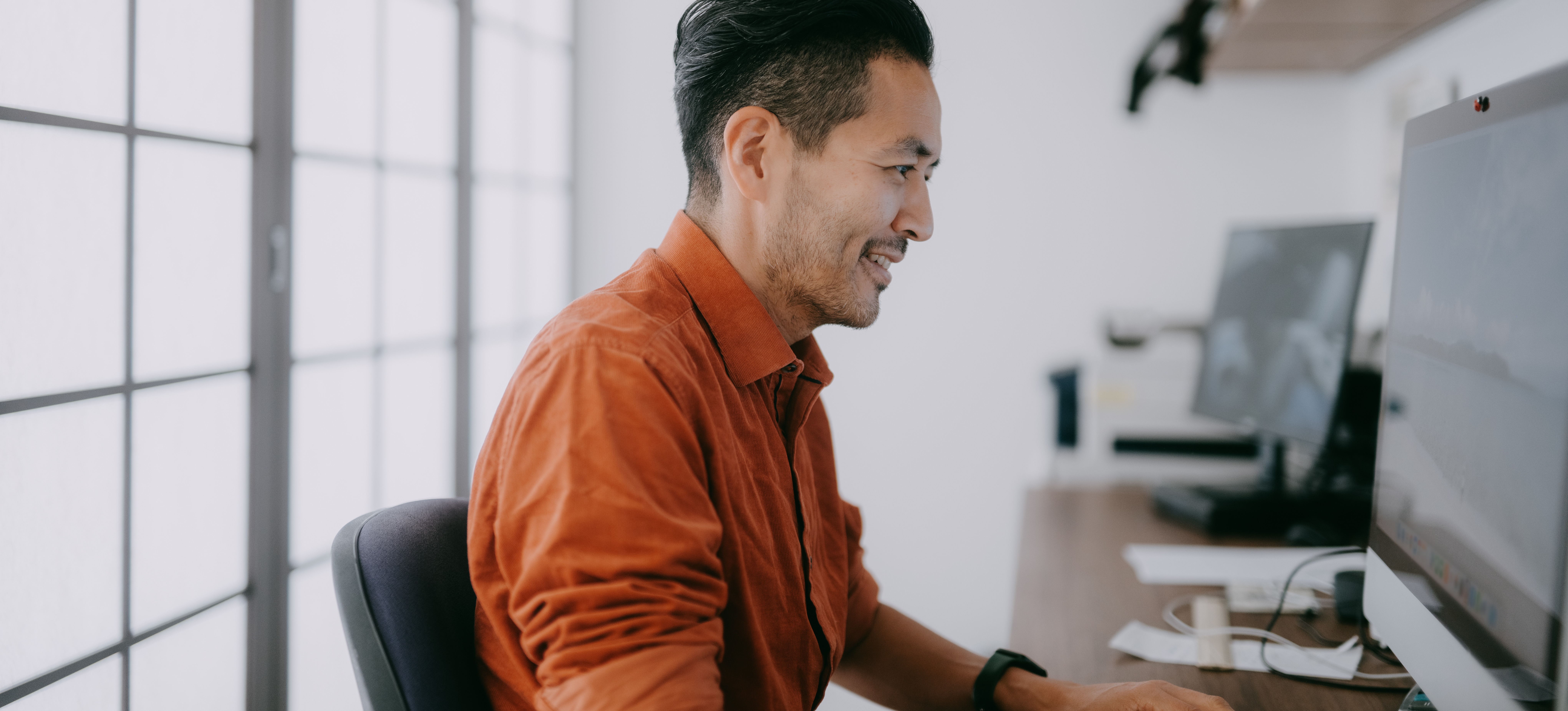 [Featured Image] A person in an orange shirt who works in service design is working on their desktop. 
