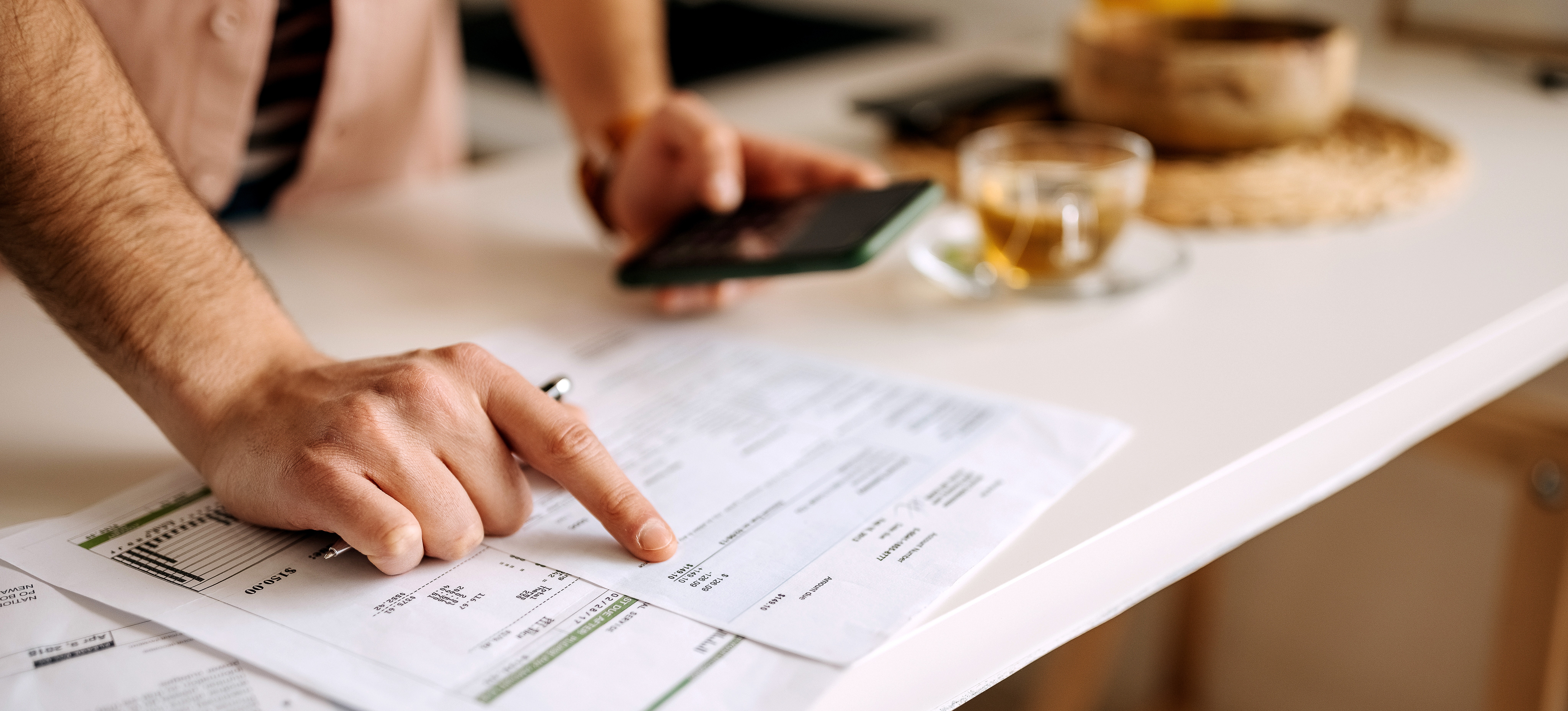 [Featured Image] A staff accountant lays financial statements on a counter and uses phone as a calculator to calculate business expenses