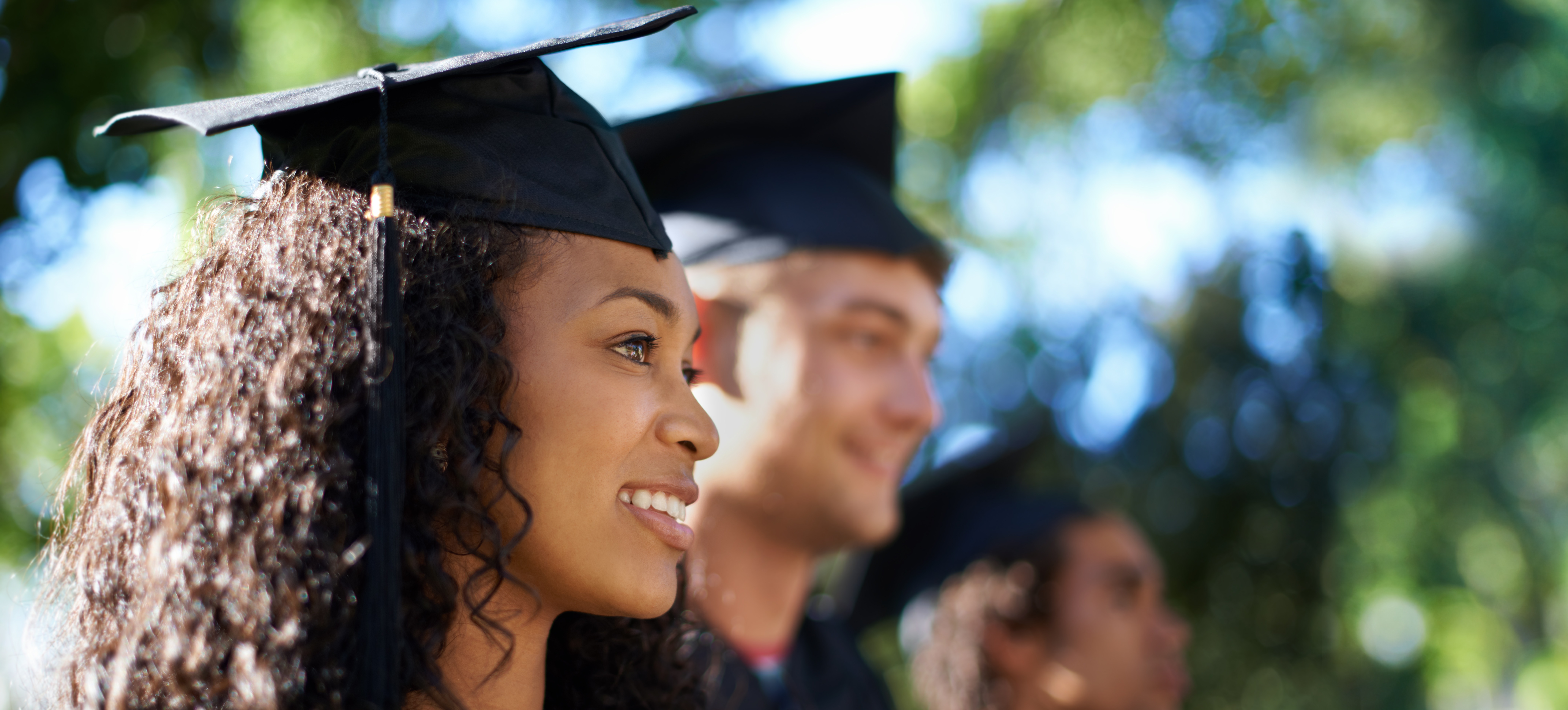 [Featured image] Graduates in caps and gowns stand outside waiting for their diplomas.
