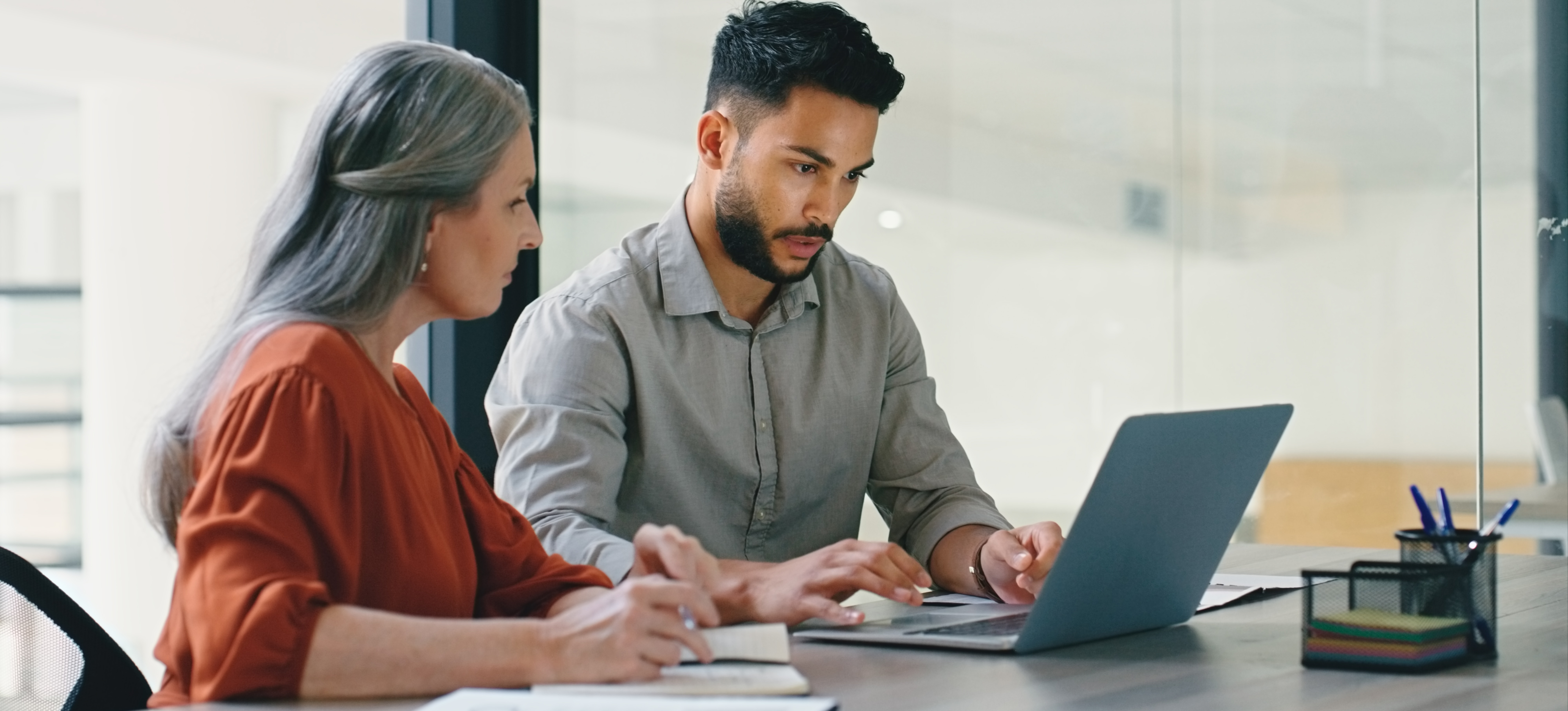 [Featured Image] A man and a woman are in an office. They are sitting at a desk looking at a computer discussing the difference between HTML and XML forms.