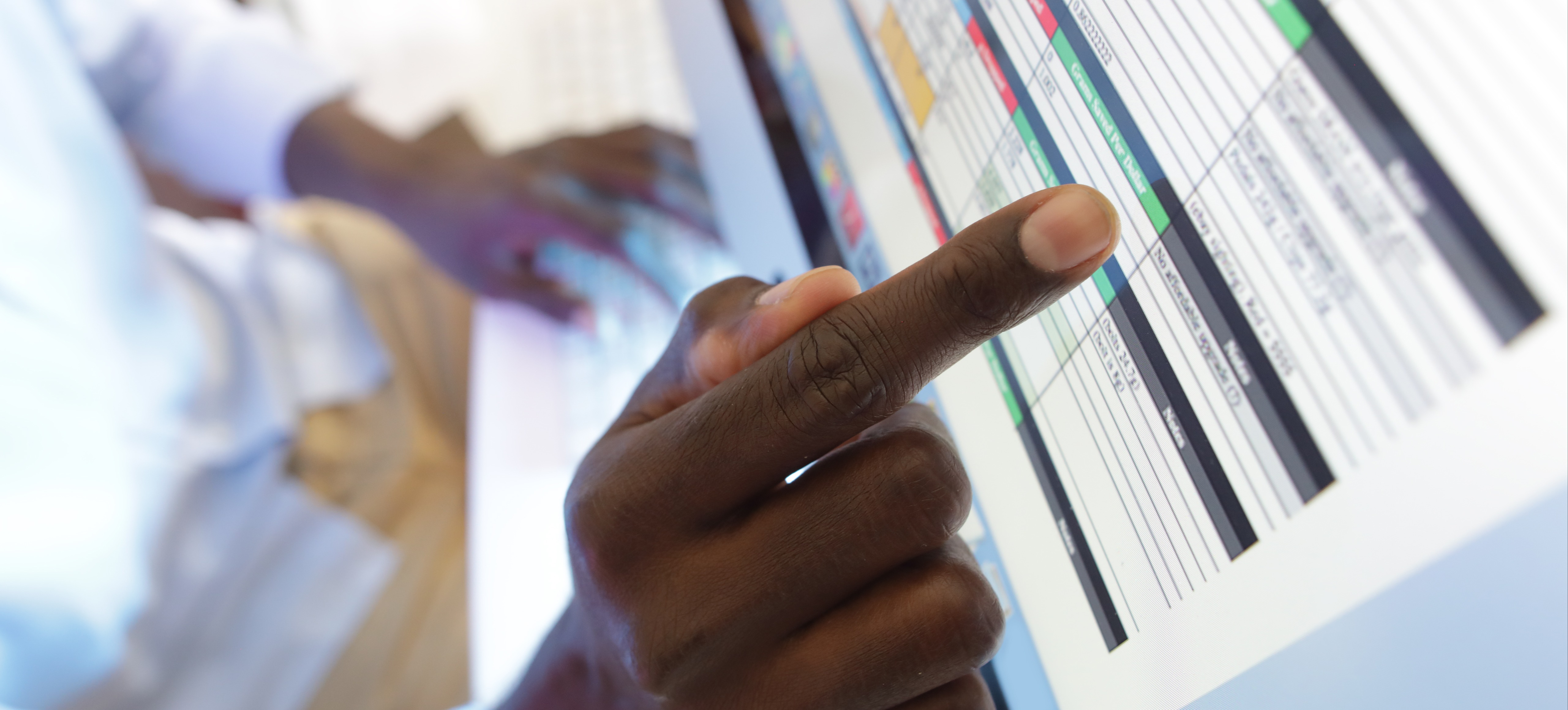 [Featured Image] A person points with their index finger to a cell in a spreadsheet on a computer monitor.
