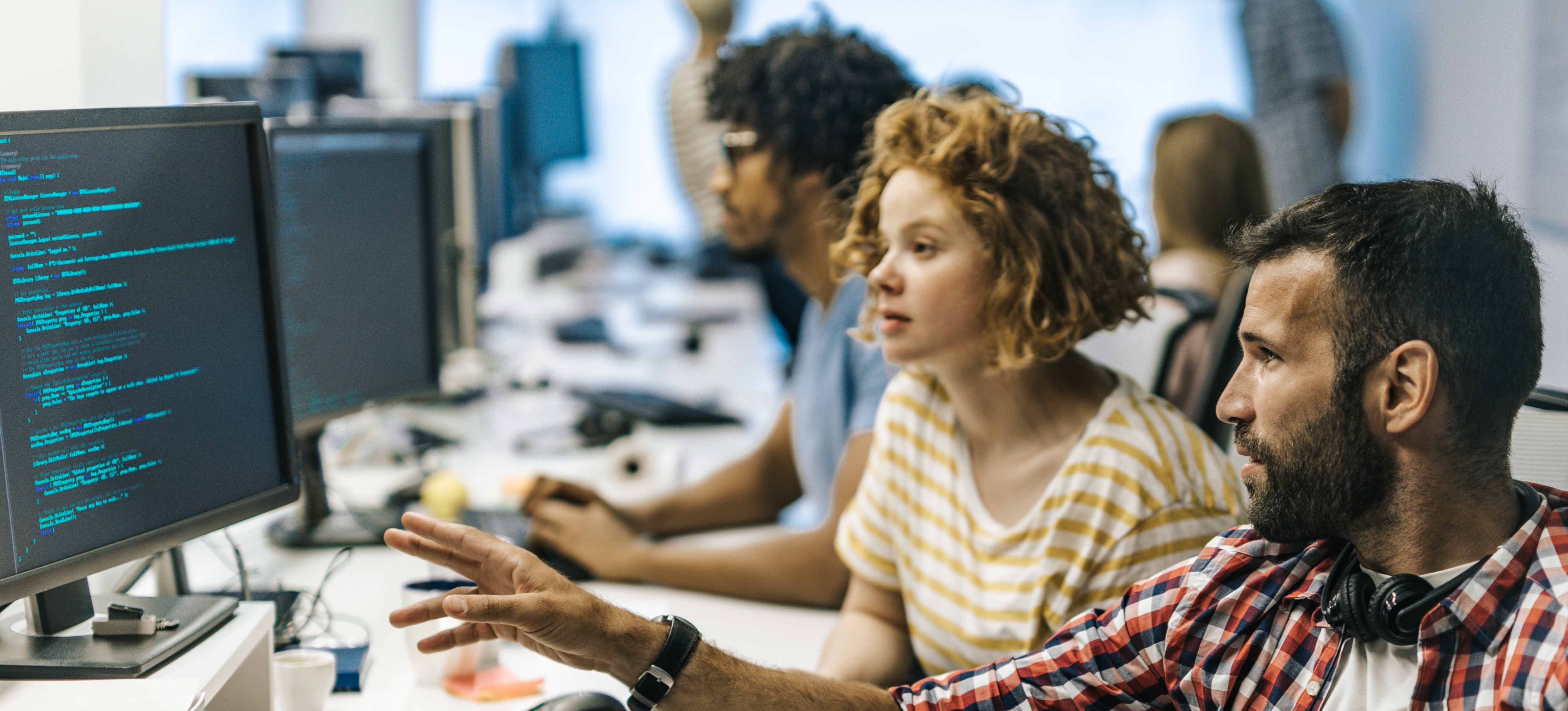 [Featured Image] Two machine learning specialists discuss dropout in neural networks as they look at a computer screen in a busy office setting.
