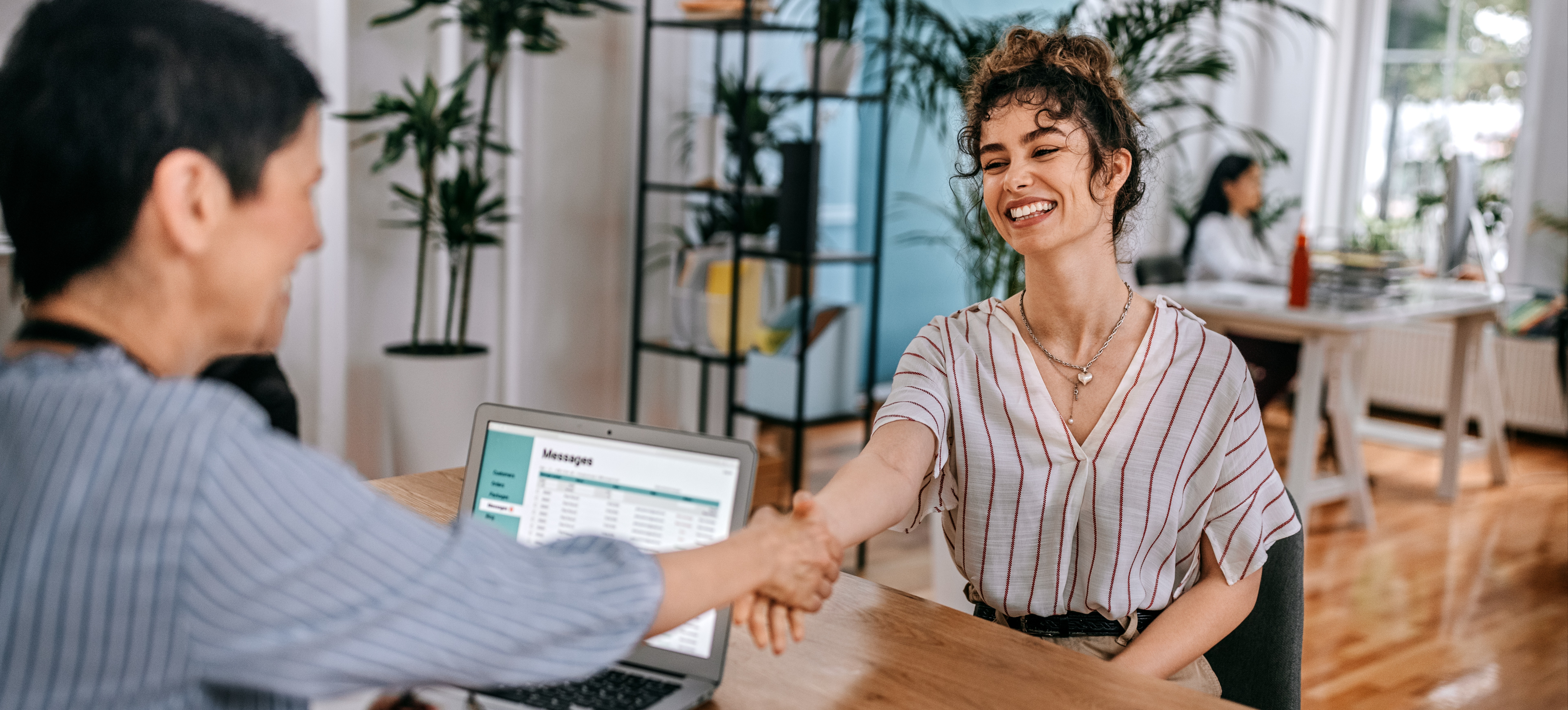 [Featured Image] Two women sit at a desk shaking hands before they start discussing iot interveiw questions in the office.