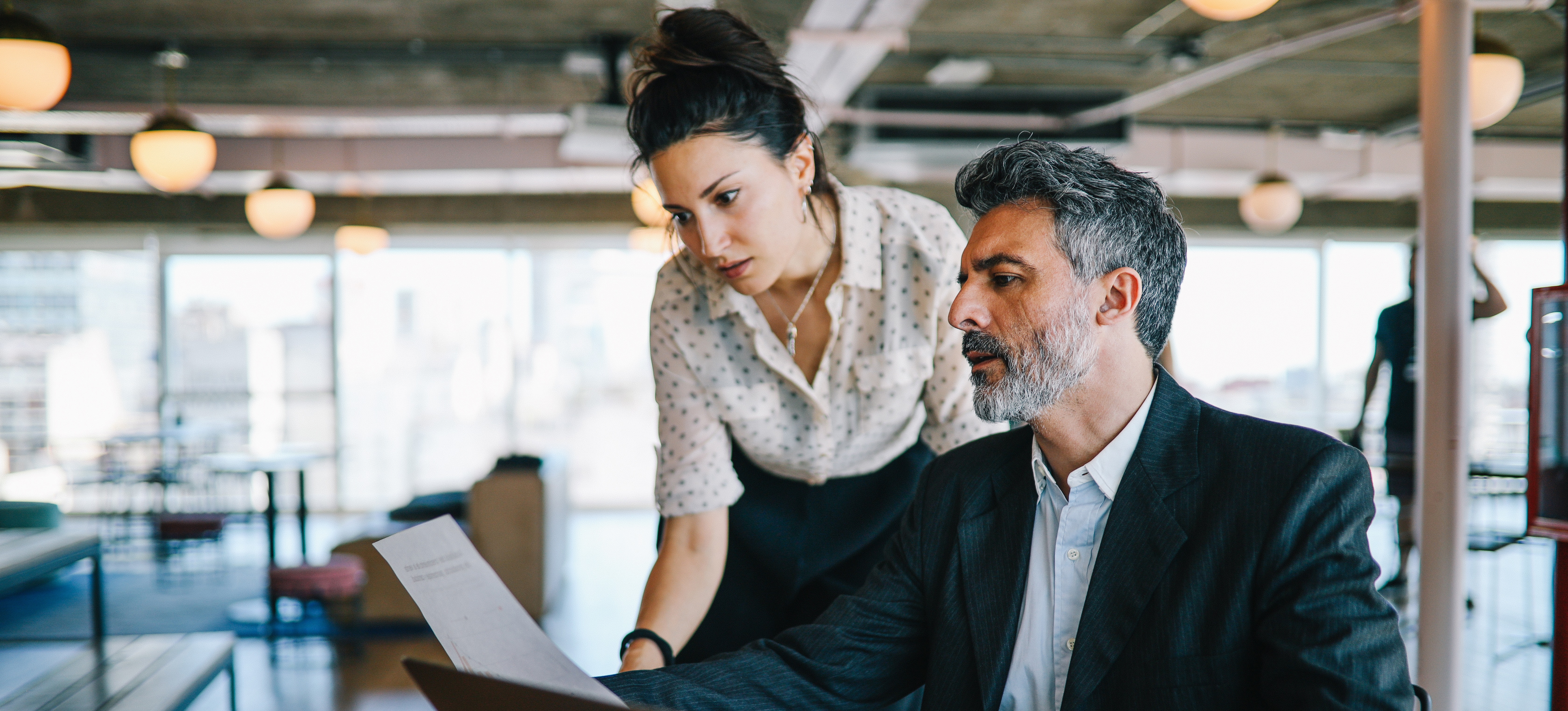 [Featured image] Two project managers review a document together in an office space using Agile