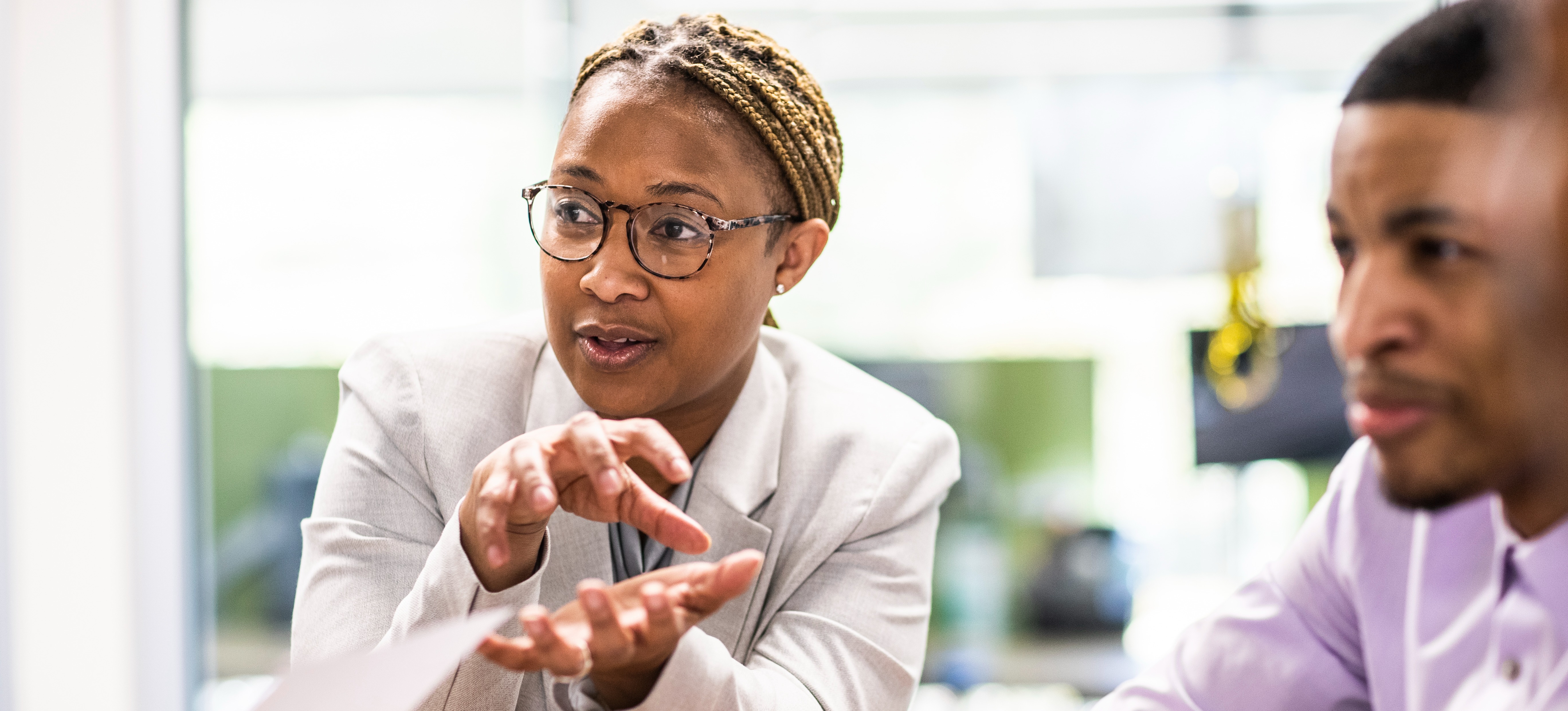 [Featured Image] A person in a suit and glasses uses their consulting skills to offer consulting services to other professionals in an office setting.

