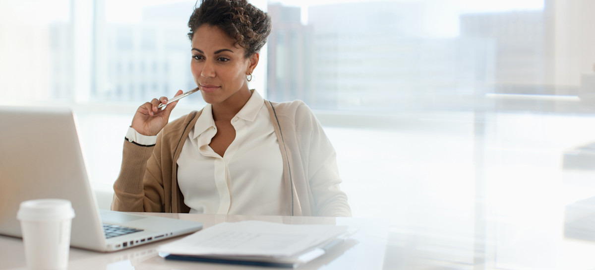 [Featured Image] A person uses their laptop and paper to draft an SQL resume in an office setting. 