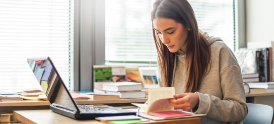 [Imagen destacada] Una aspirante a gestora de proyectos hojea varios libros de gestión de proyectos mientras estudia para el PMP.