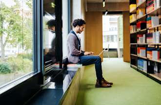 [Featured image] A data analytics degree student works on his laptop in a university library.