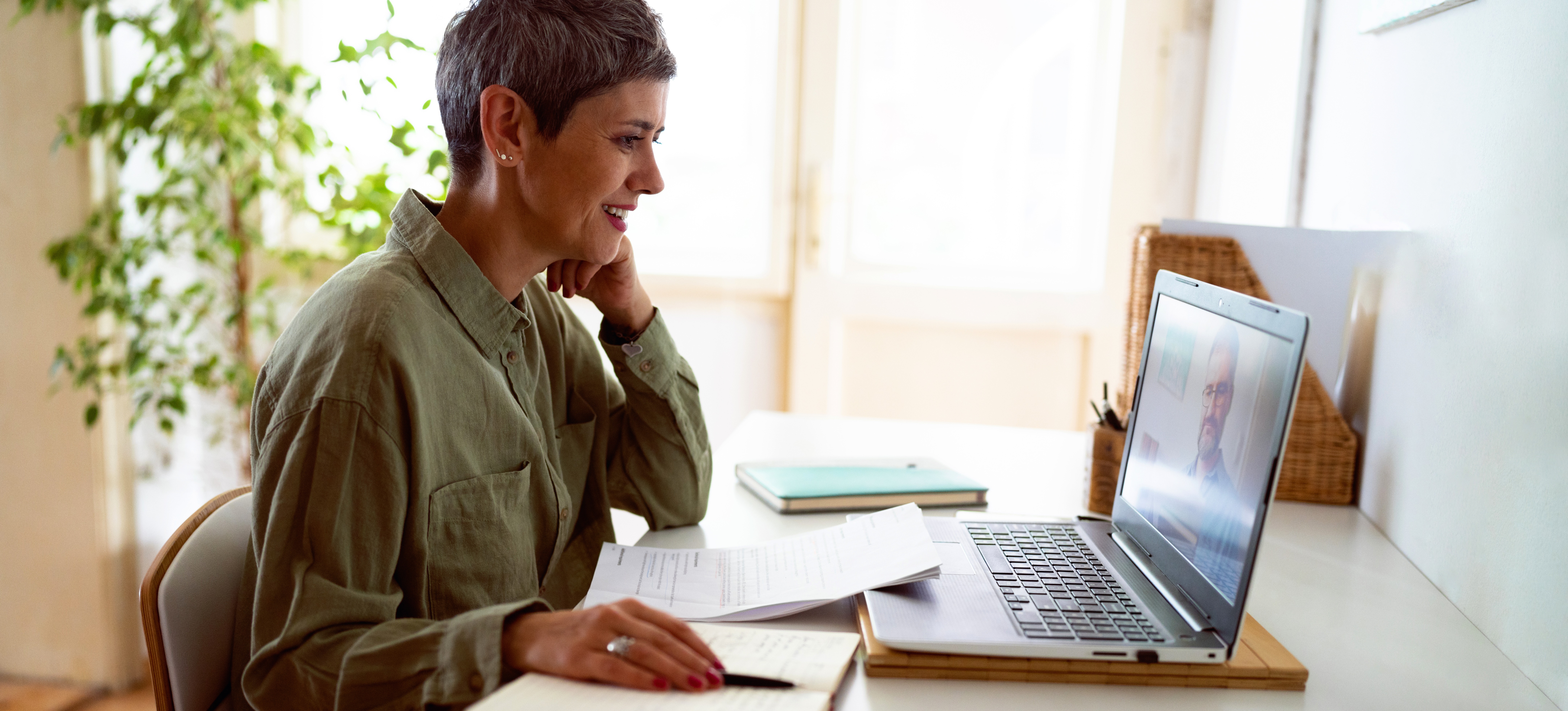 [Featured Image] A woman in a green shirt sits at a table with a laptop and notebooks and participates in a corporate online learning and development program.