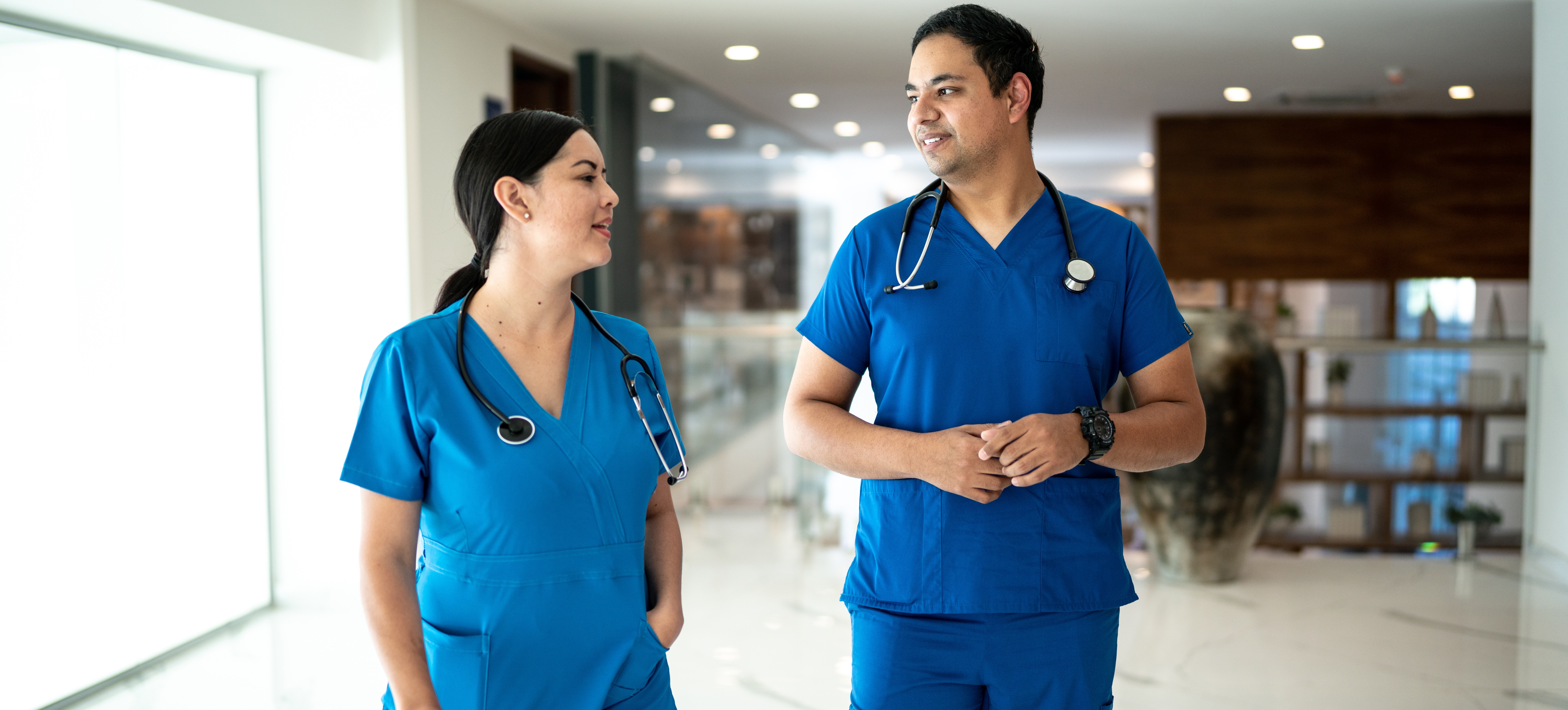 [Imagen destacada]: Dos enfermeras conversan en un hospital, destacando la importancia de un título en enfermería para trabajar en equipo y brindar atención de calidad.