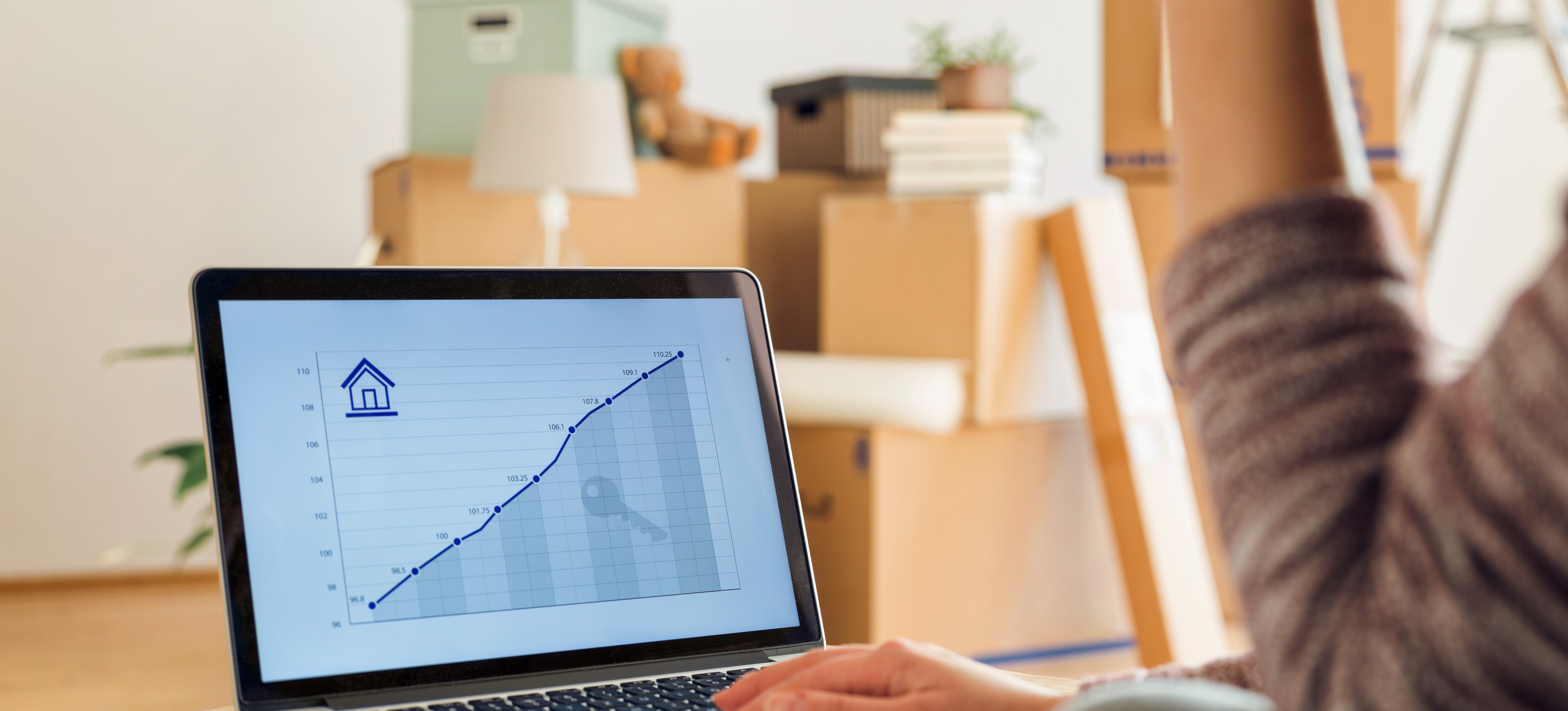 [Featured Image] A person who is moving into a new home looks at a real estate line graph on a laptop.