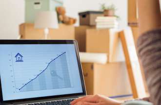 [Featured Image] A woman who is moving into a new home looks at a real estate line graph on a laptop.