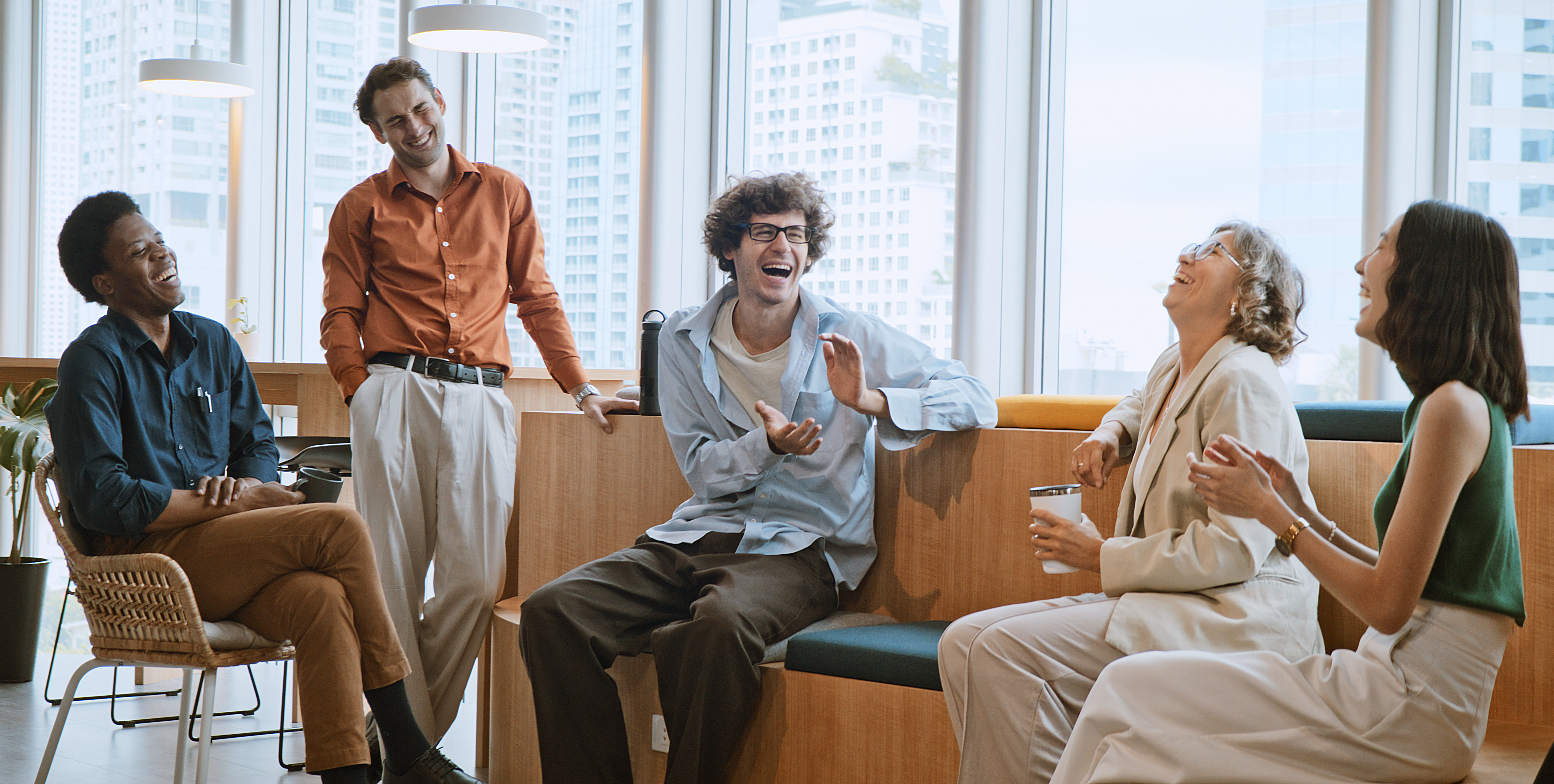 [Featured Image] A group of laughing colleagues sit together in an office and work on team-building skills as part of employee development.