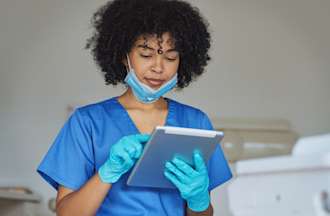 [Featured Image] A dental hygienist looks at a tablet. 