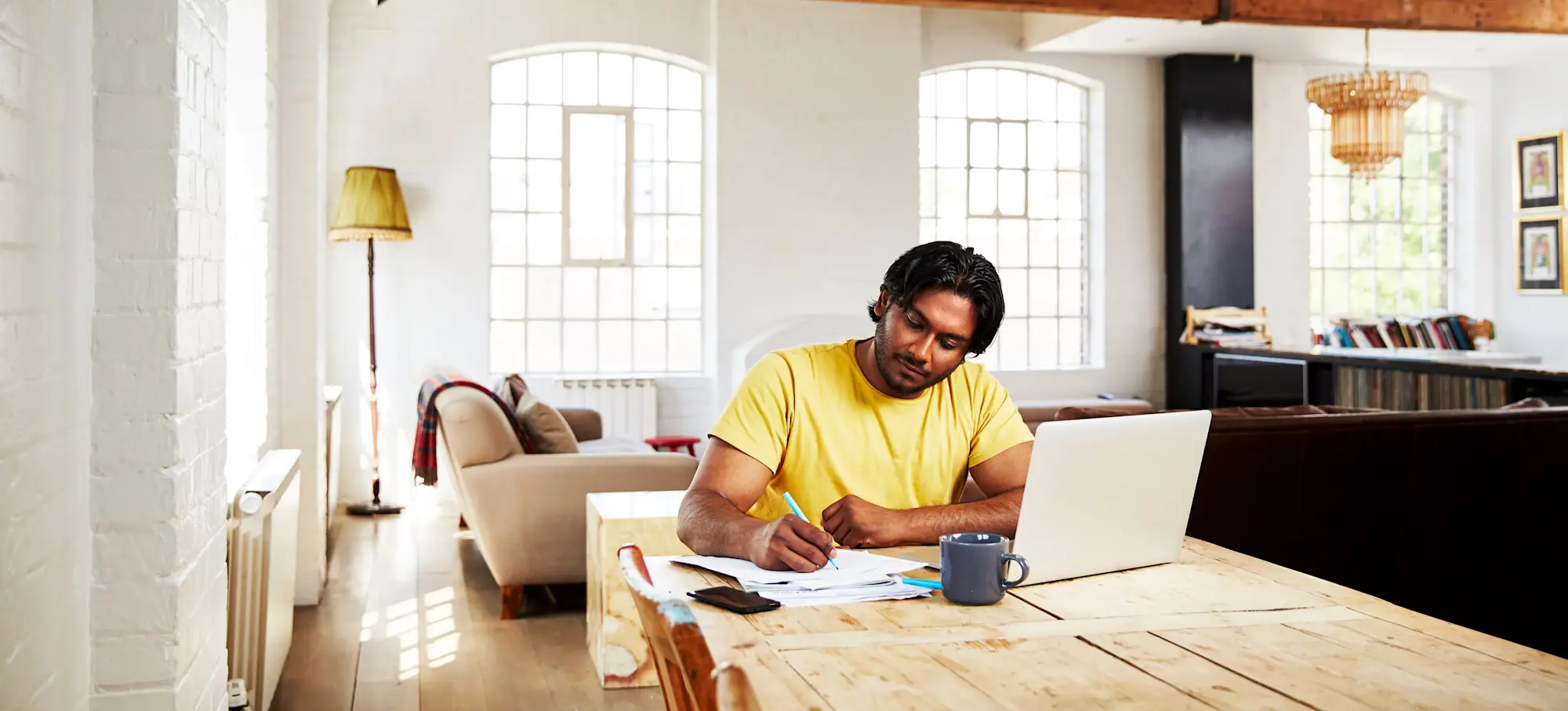 [Featured Image]: A man sits at a dining table writing on a tablet as he considers side jobs to make extra money.