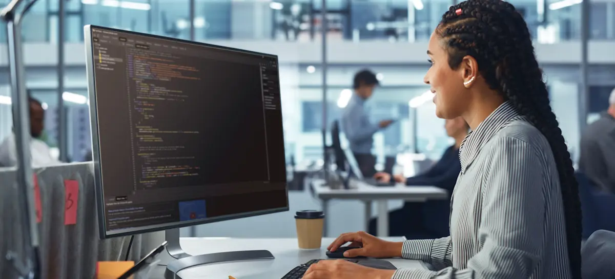 [Featured Image] A person works at a desktop computer in an office, comparing Java and C++.