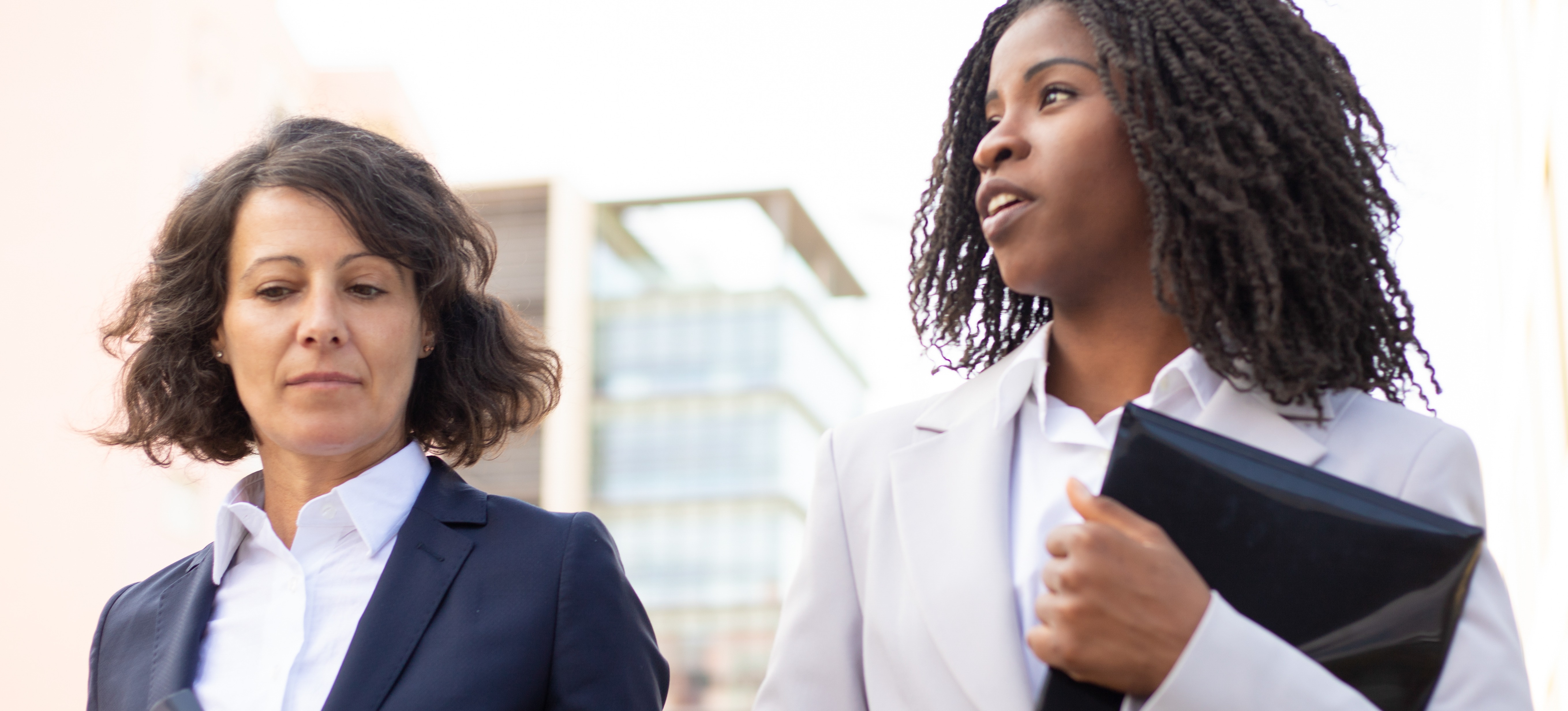 [Featured Image] Two cyber threat analysts carry folders and walk from the parking lot to their CIA cybersecurity jobs. 
