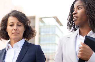 [Featured Image] Two cyber threat analysts carry folders and walk from the parking lot to their CIA cybersecurity jobs. 
