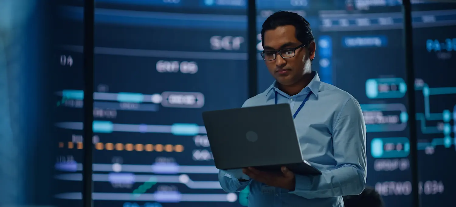 [Featured image] A cybersecurity analyst enacts measures backed by the CIA triad framework. They're holding a laptop and standing in a dark server room.