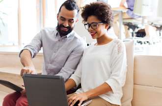 [Featured image] Two coworkers sit on a wooden bench and collaborate using Active Directory on a laptop.