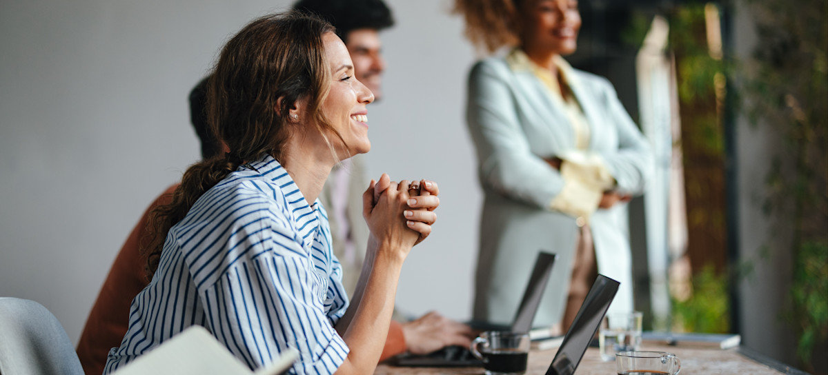 [Featured Image] A learner sitting in front of a laptop smiles as they listen to their in-person instructor, all part of the blended learning program they enrolled in.