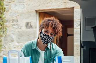 [Featured Image]:  A female, wearing a green jacket, a white shirt, and a face covering, is putting drugs in a basket, performing duties as a public health intern, 