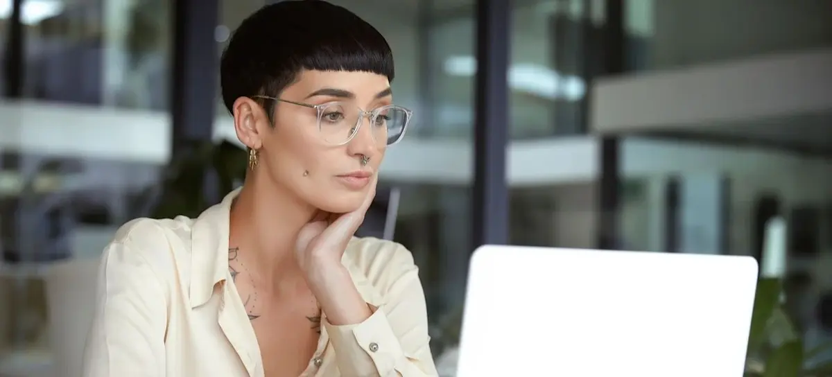 [Featured Image] A person in business casual clothing sits at a desk using their laptop.