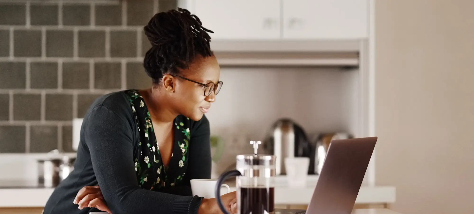 [Featured Image] A professional researches the average data visualization salary on a laptop while in their kitchen as they plan a potential career change.
