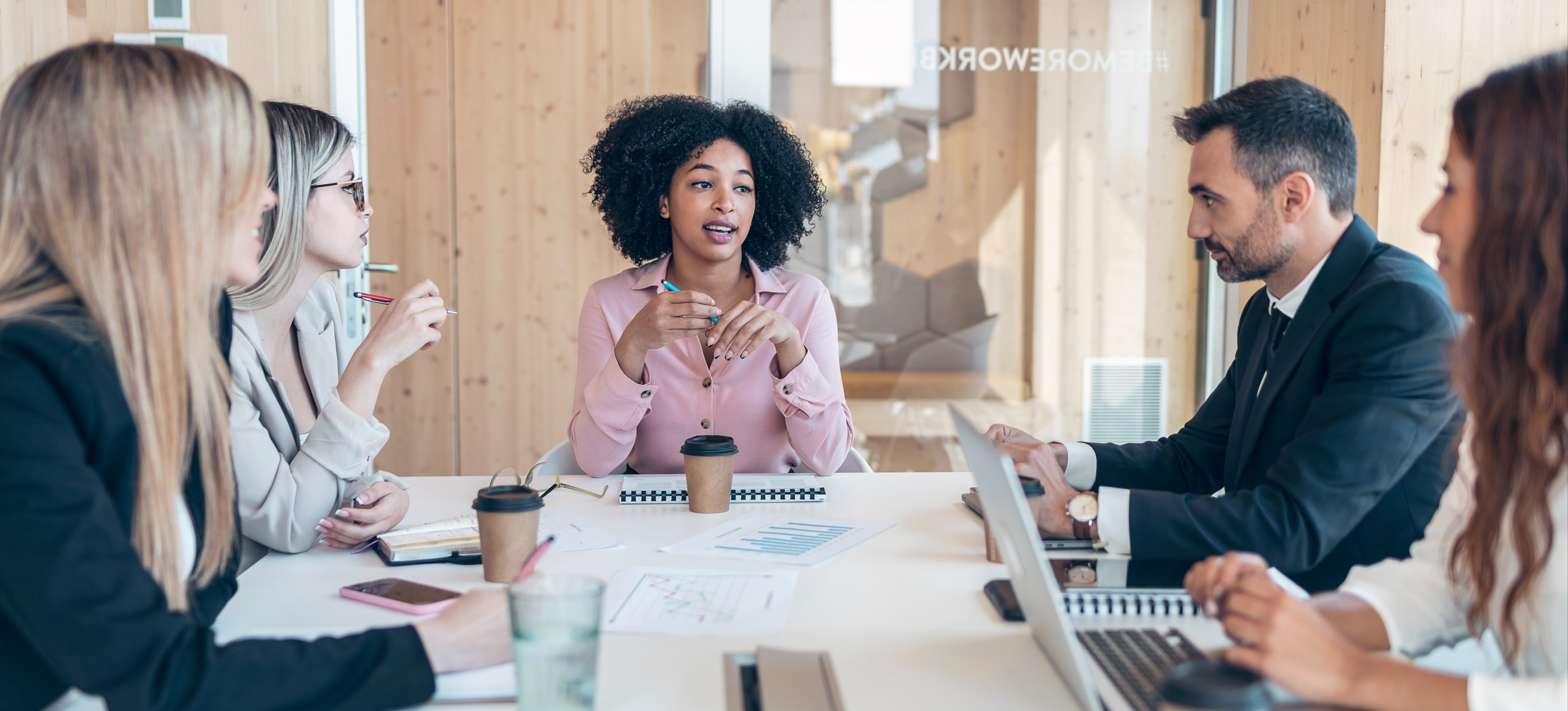 [Featured Image] A group of professionals in a meeting room, discussing task automation strategies with documents on the table, collaborating in a structured business environment.
